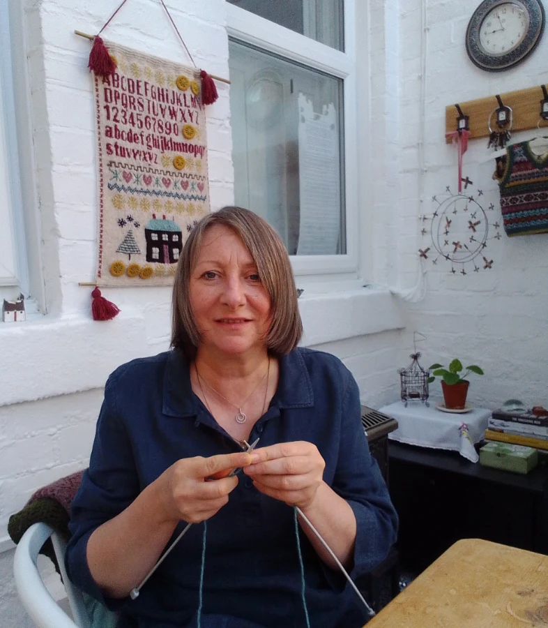 Lynn Hall doing some knitting with one of her final assessment pieces proudly on display in the background